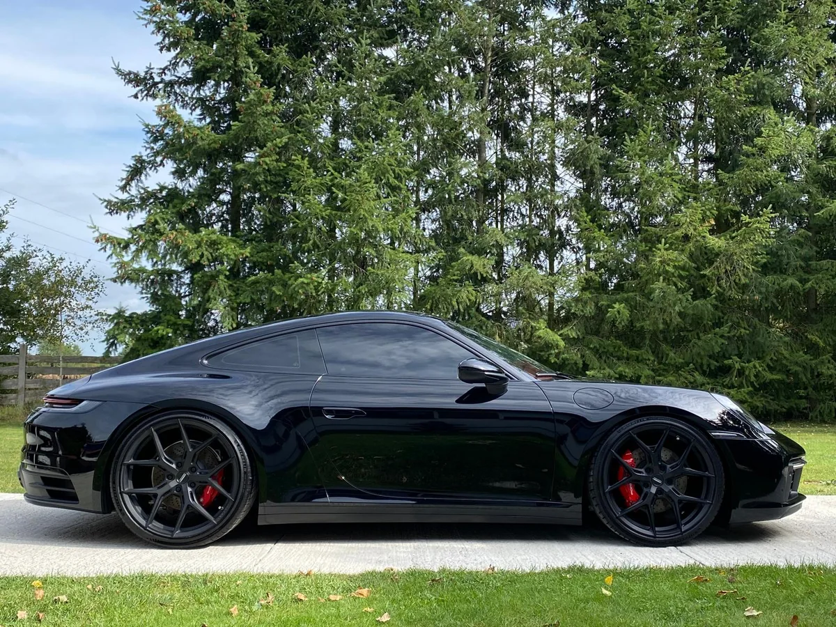 Czarne Porsche 911 z boku, odbicia w lakierze i czerwone zaciski